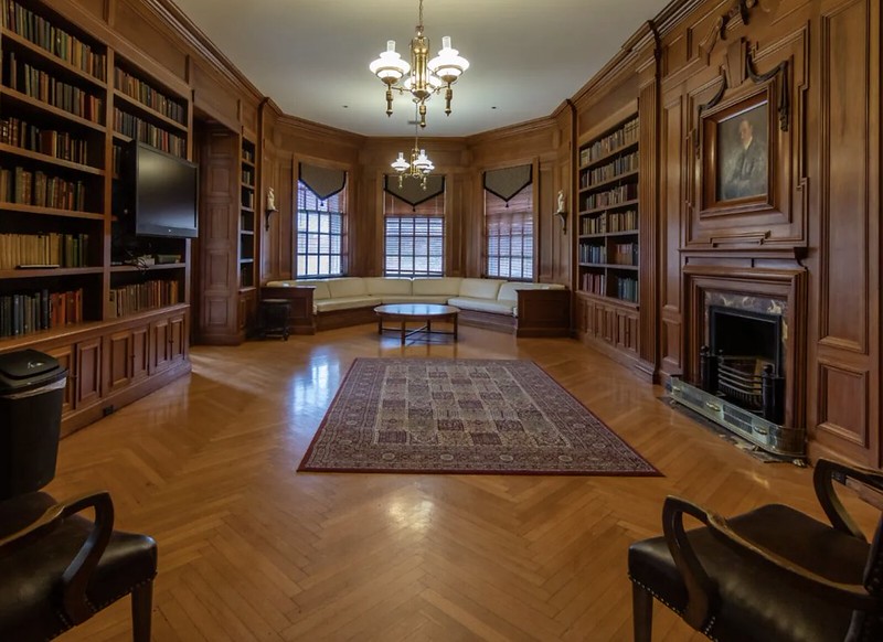 large room with 3 windows, a wooden floor and built in book shelf, and fireplace