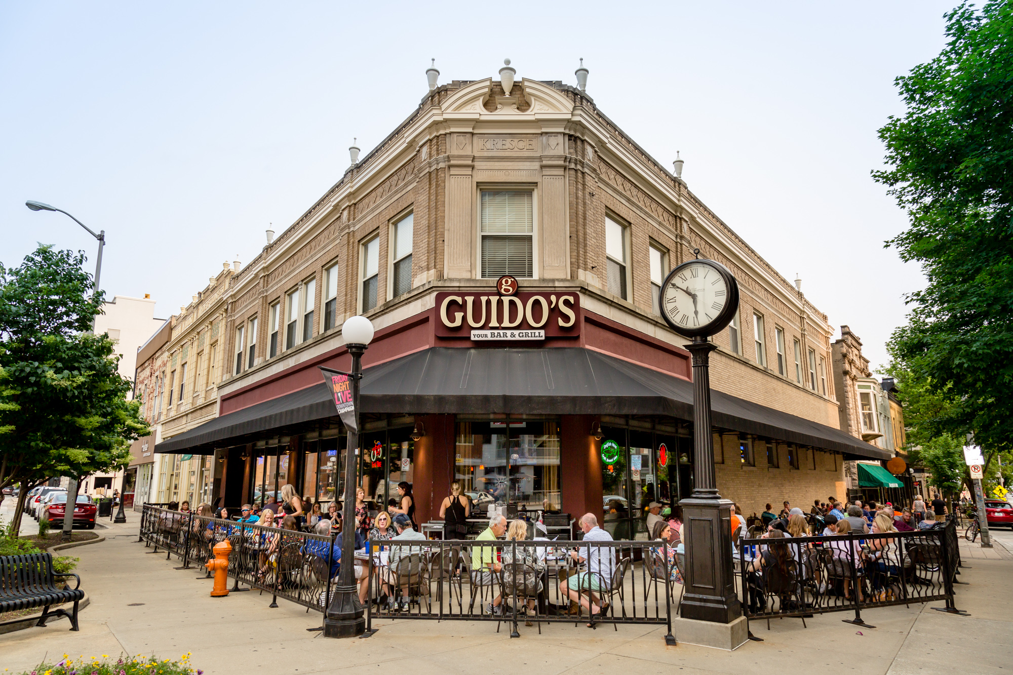 brick restaurant with outdoor seating, a canopy, and an outdoor clock