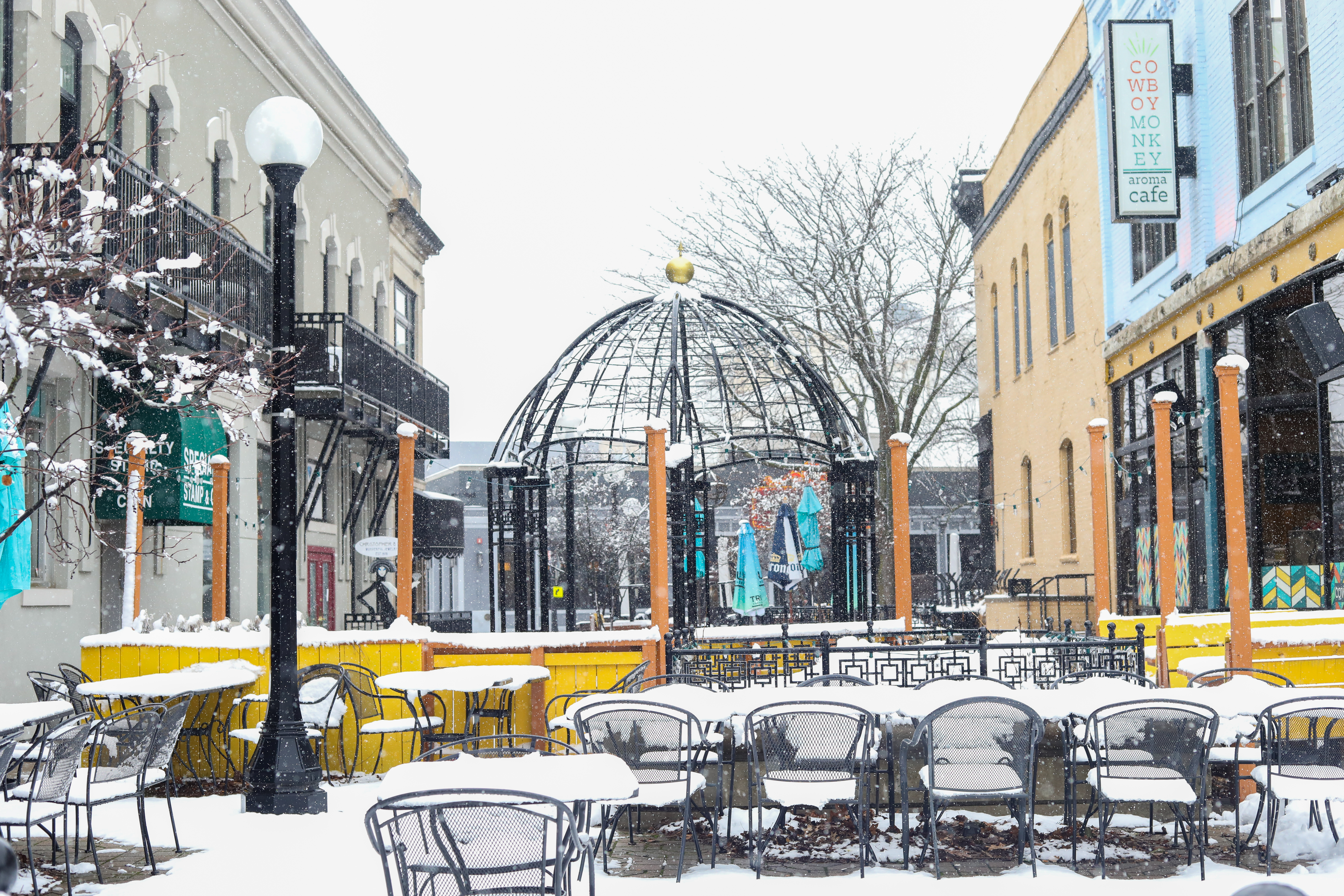 outdoor seating area covered in snow, surrounded by downtown buildings