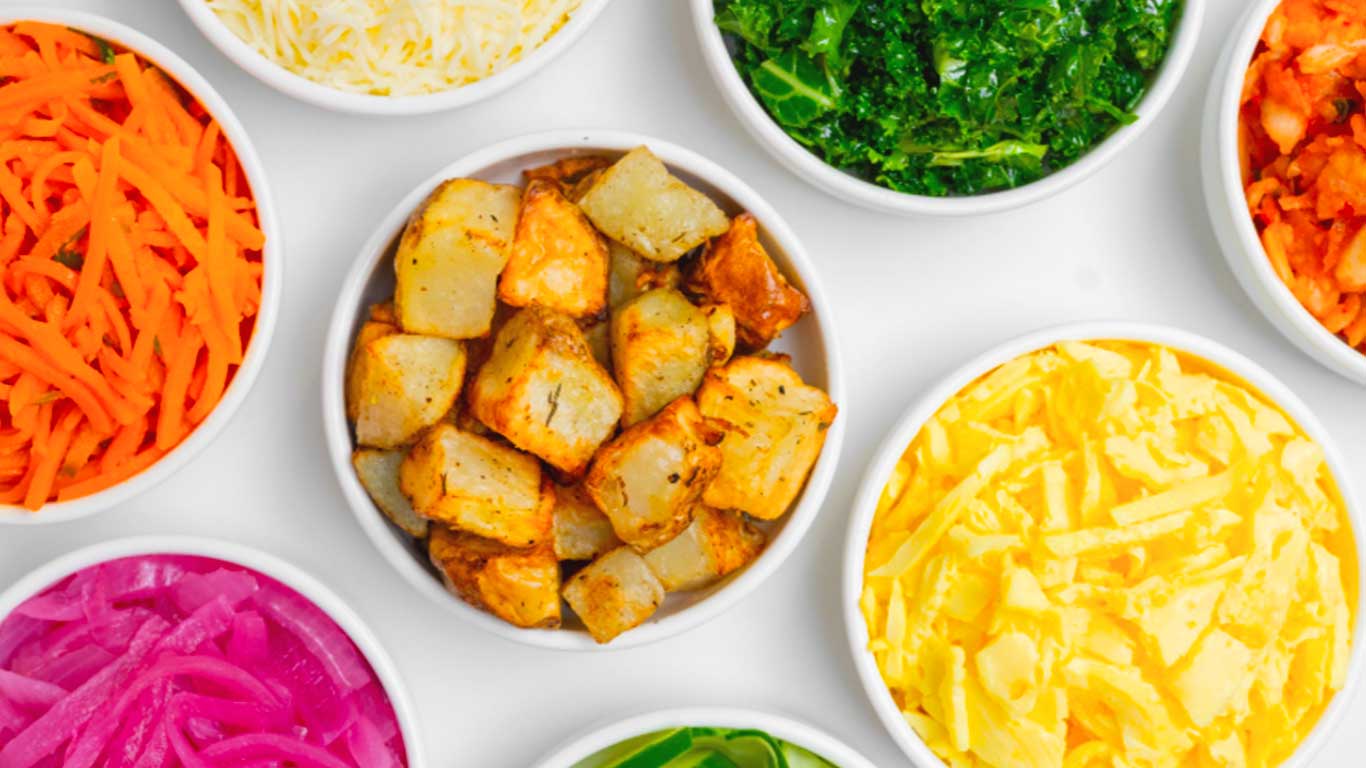 Numerous white bowls filled with colorful food such as purple cabbage, kale, carrots, and more