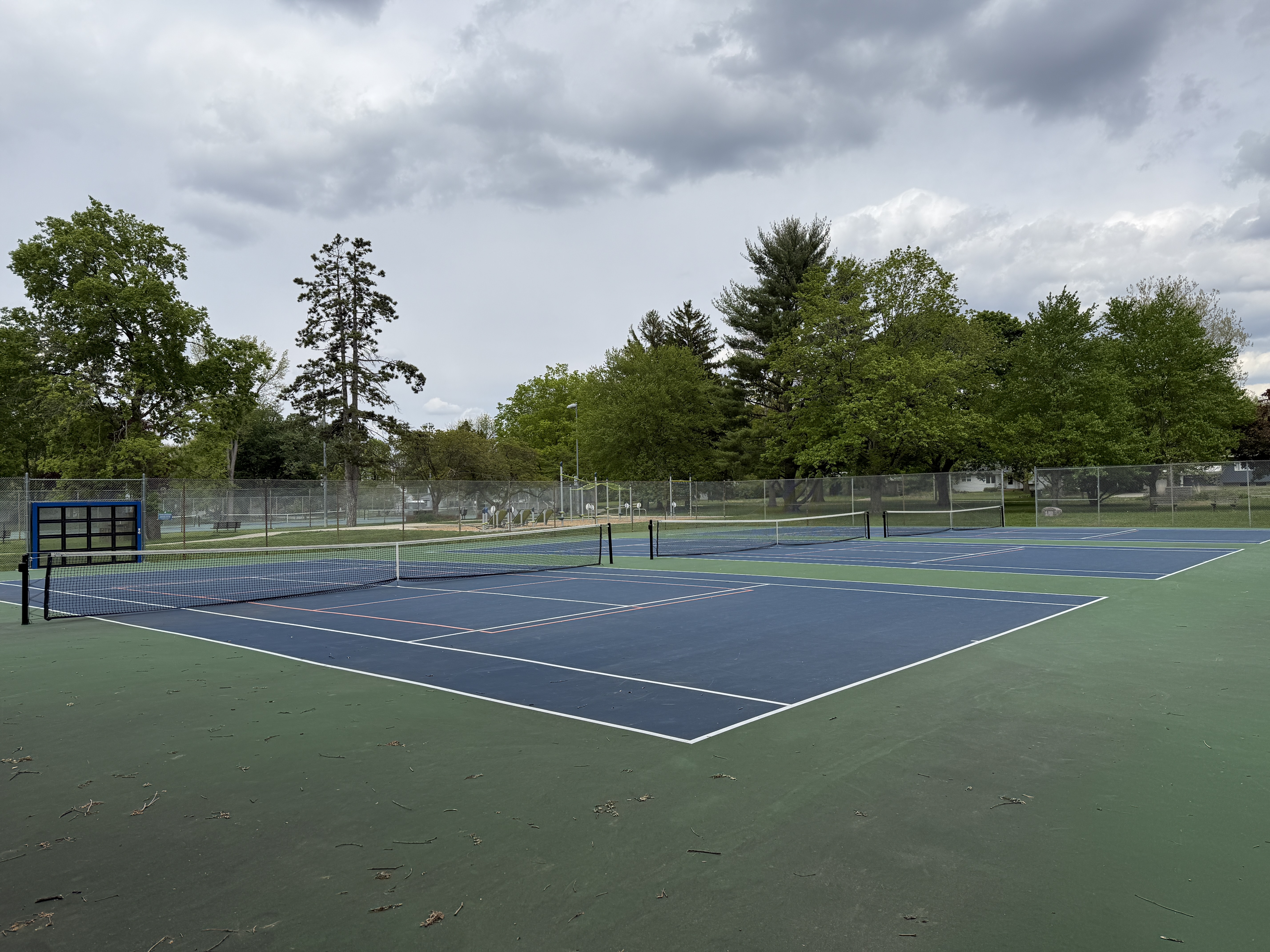 blue and green tennis courts with trees in the background