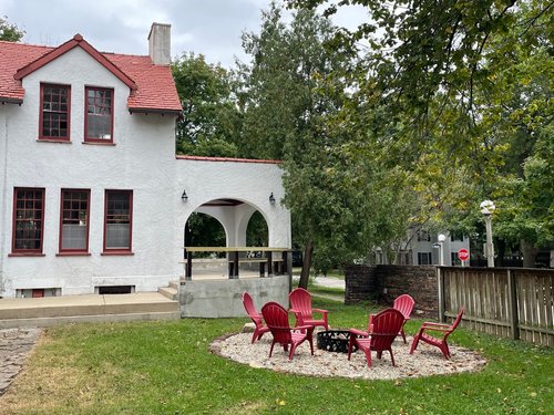 white stucco house with rust-colored roof and outdoor chairs in the yard