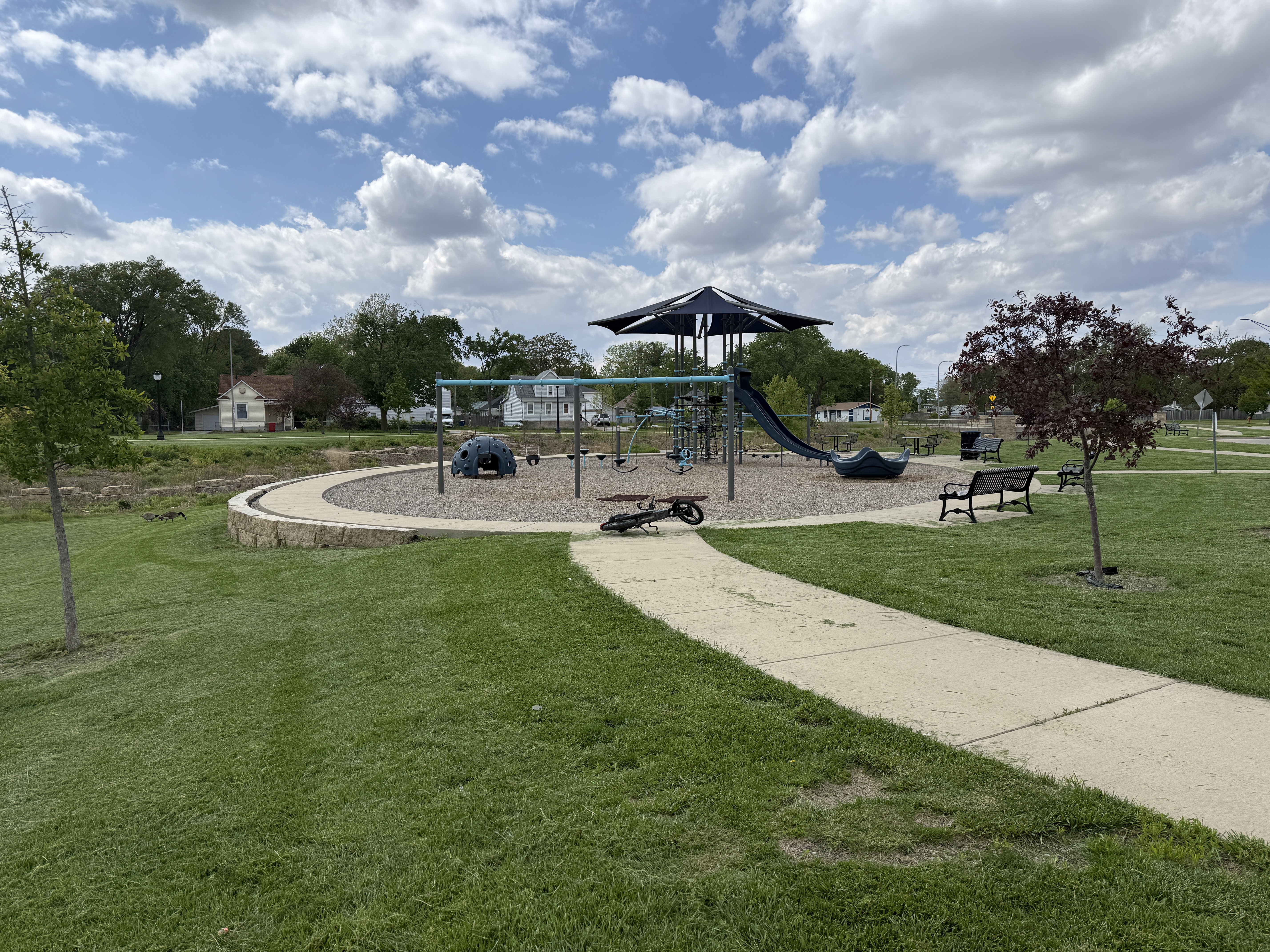 Circular playground, surrounded by grass, with a walking path