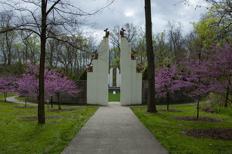 cream-colored entry statue between purple flowers with a walkway and trees