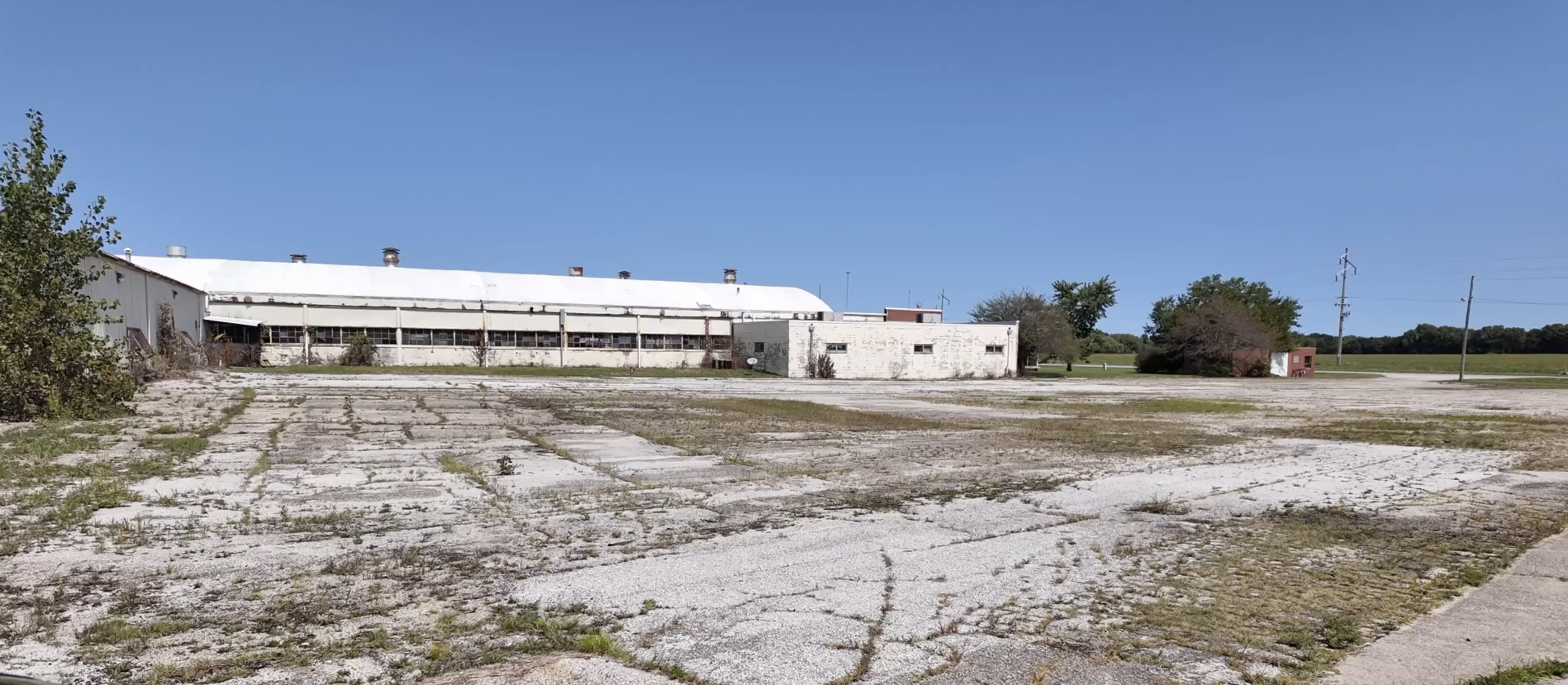 exterior of large, off-white building with rows of windows and an overgrown parking lot