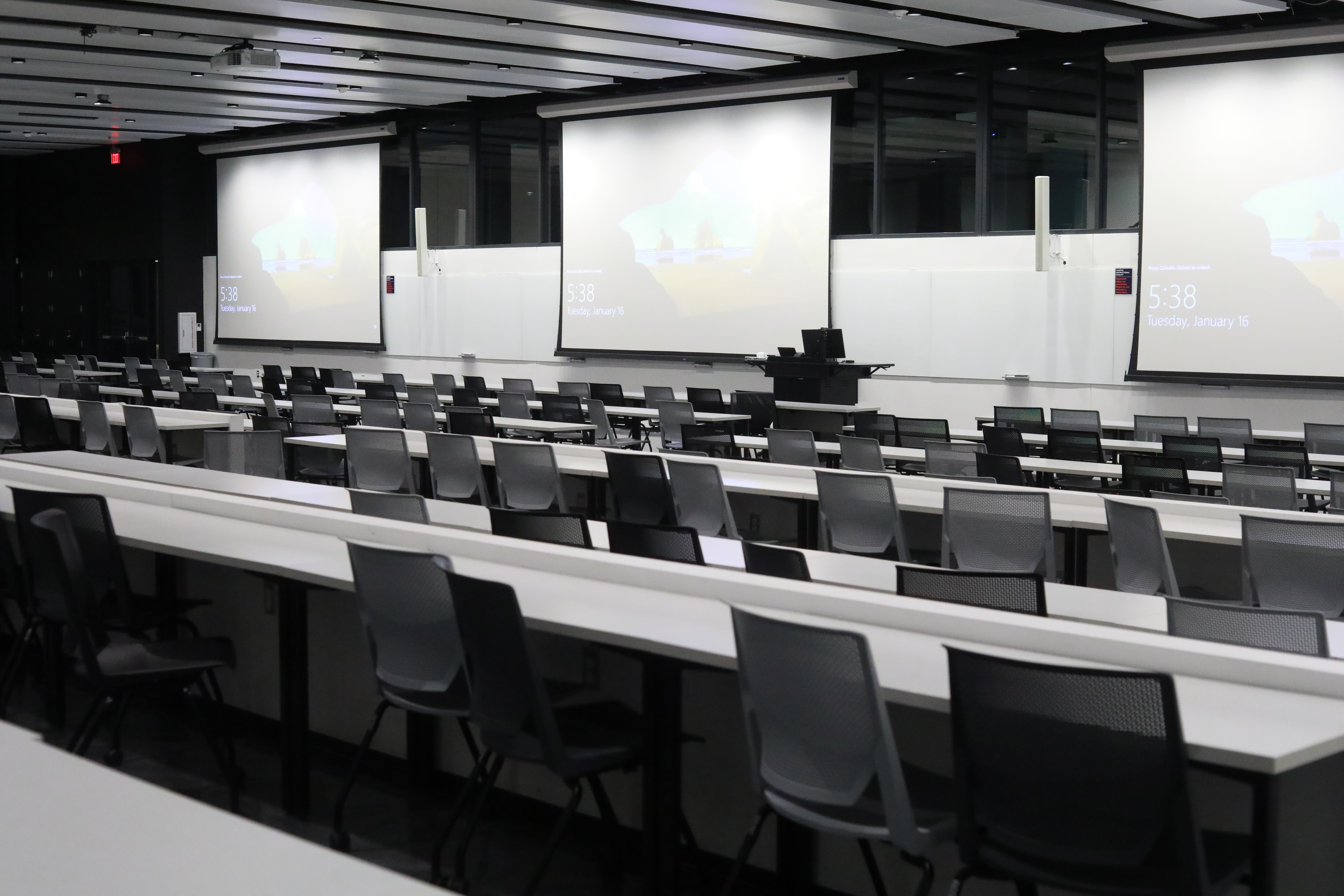 Classroom with front-facing tables and chairs and projector screens