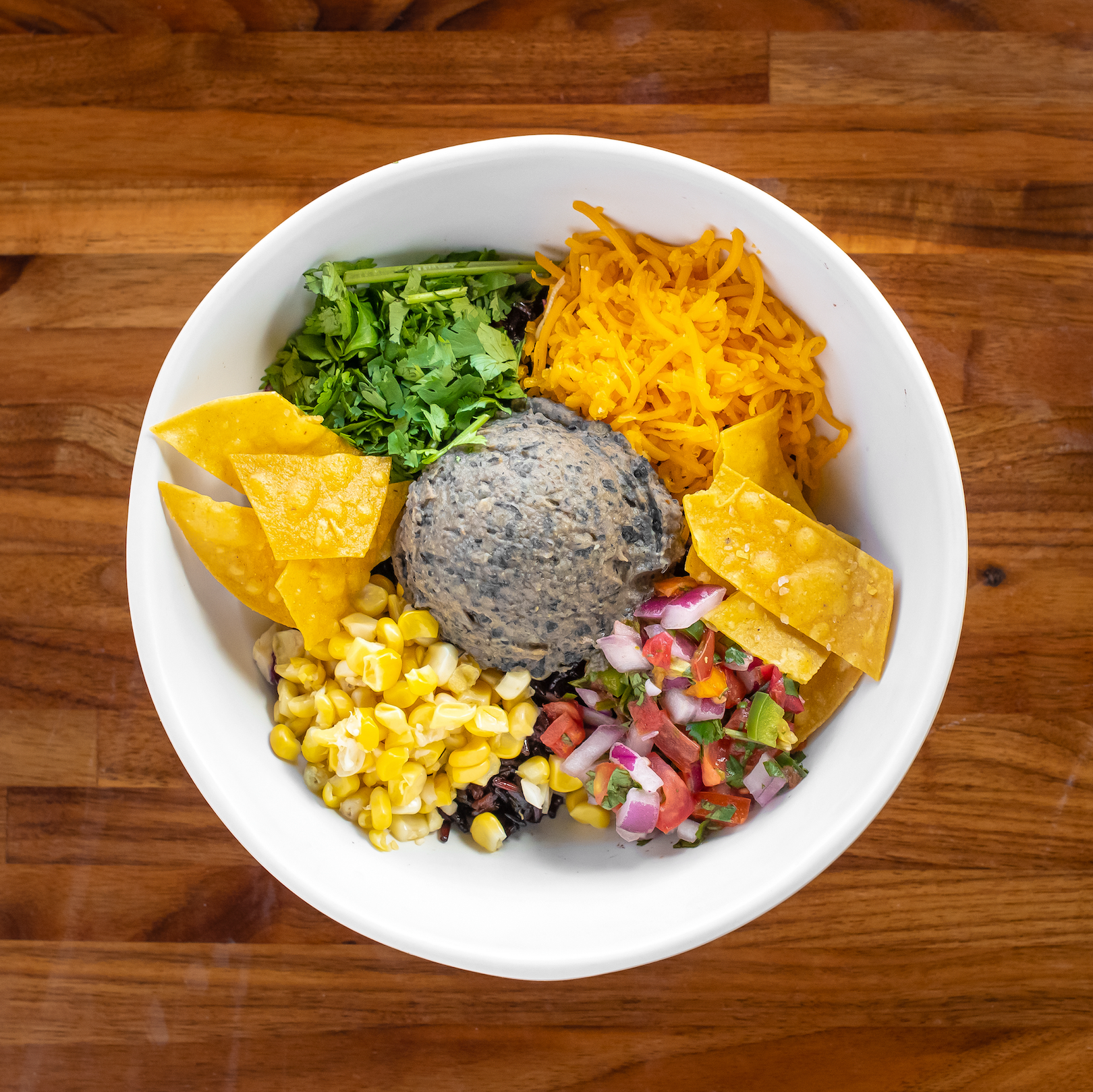 Fiesta bowl with tortilla chips, cilantro, corn, pico, cabbage slaw, cheese, and bean dip di gallo,