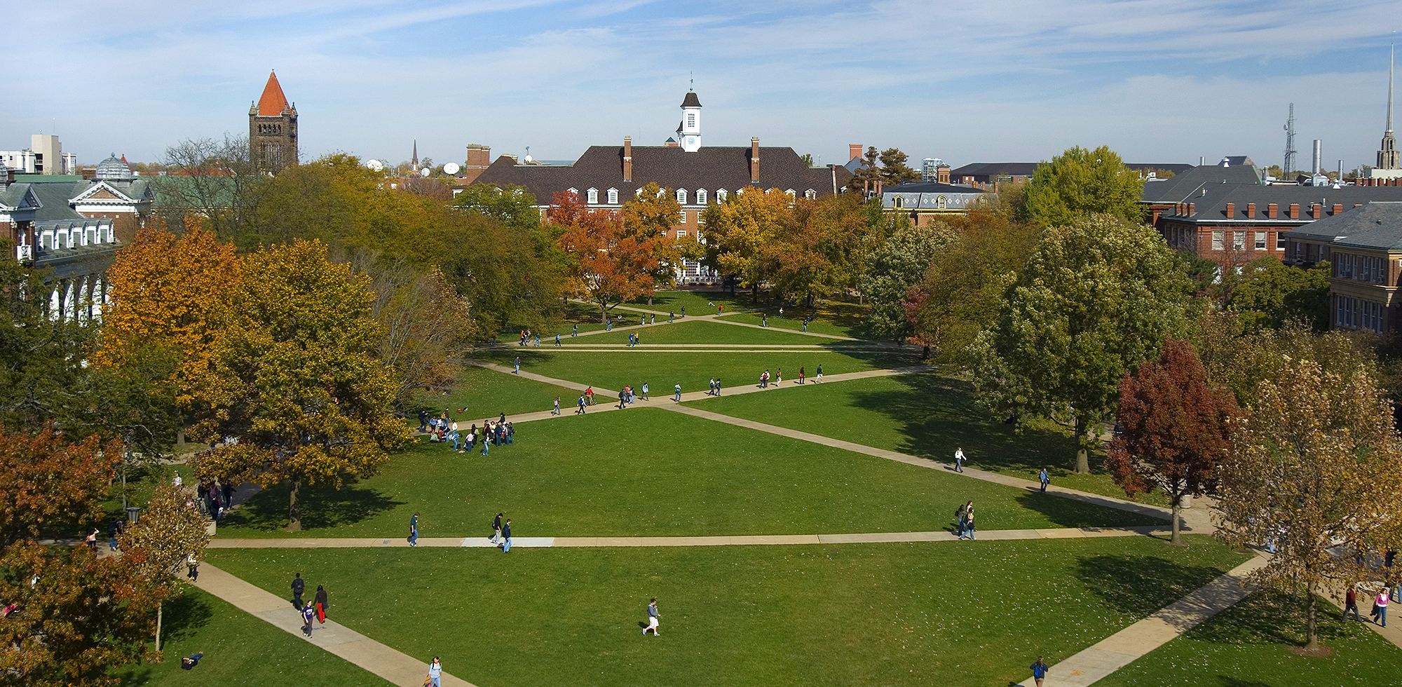 large green space with x-shaped walkways, surrounded by trees and buildings