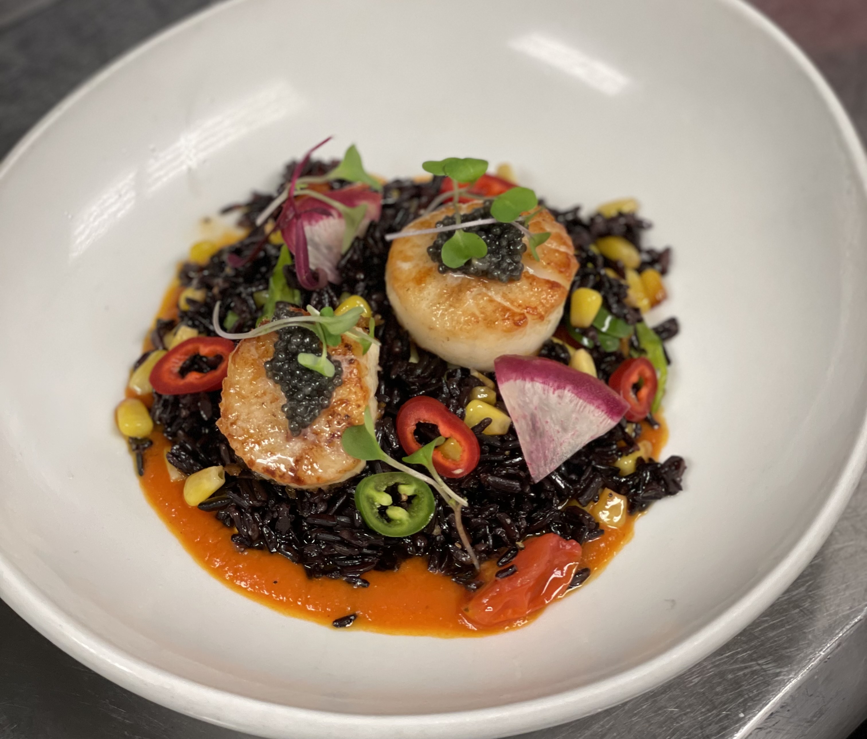 Seared scallops atop black risotto, topped with fresh vegetables