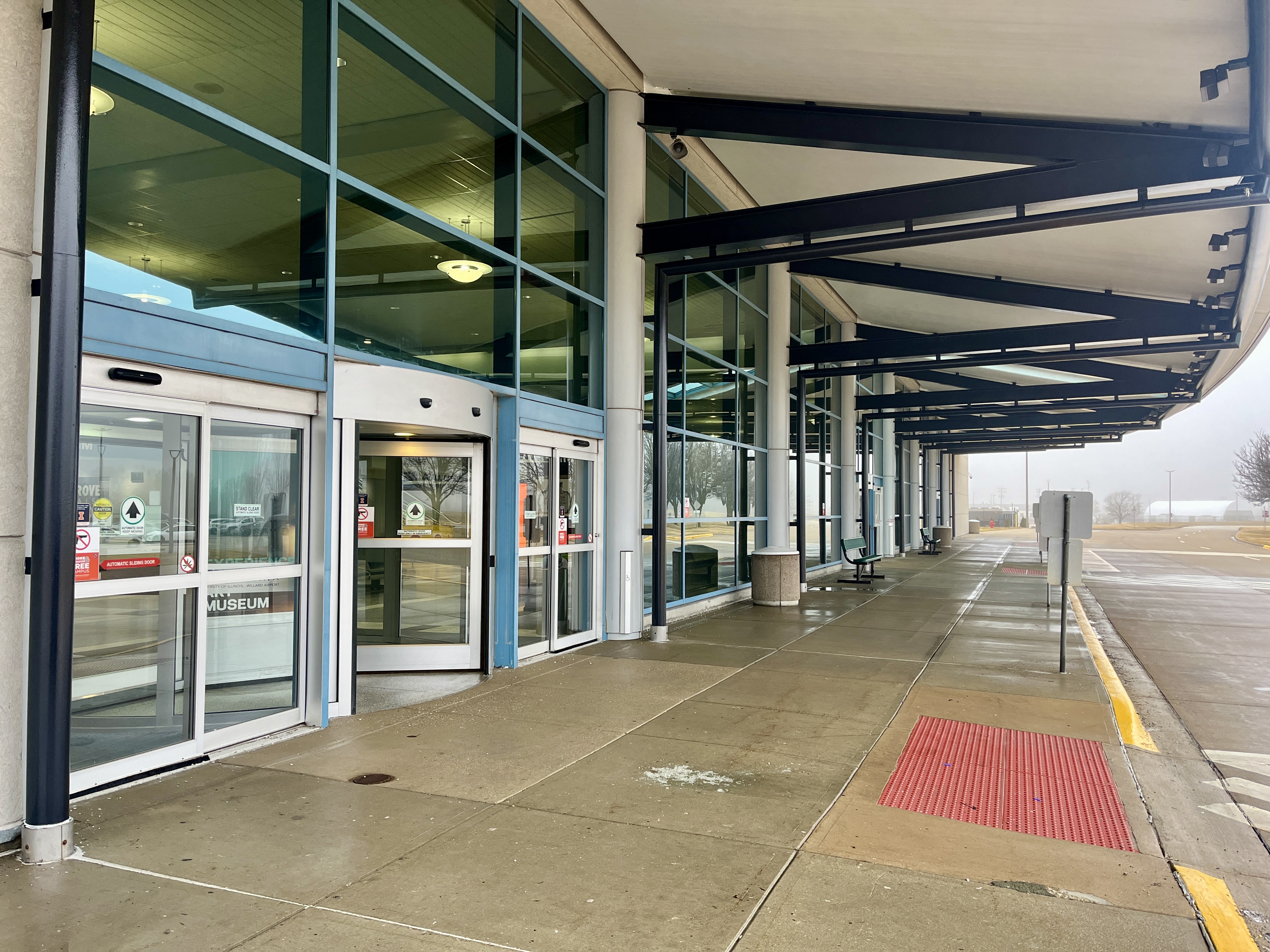 exterior airport entrance with automatic doors, tall windows, and a sidewalk