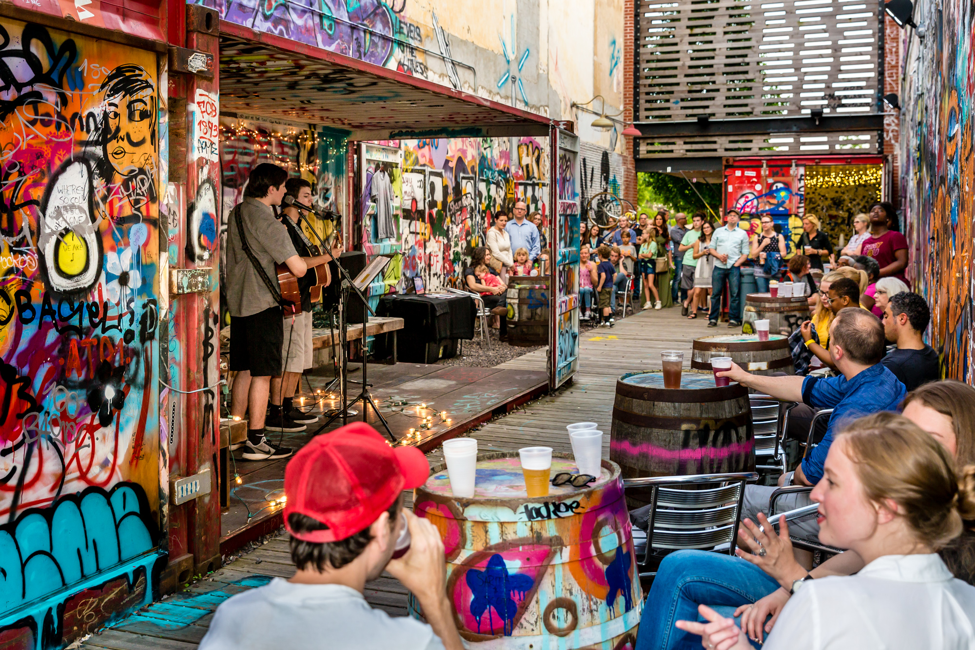 musicians playing at an outdoor urban stage with graffiti and spectators