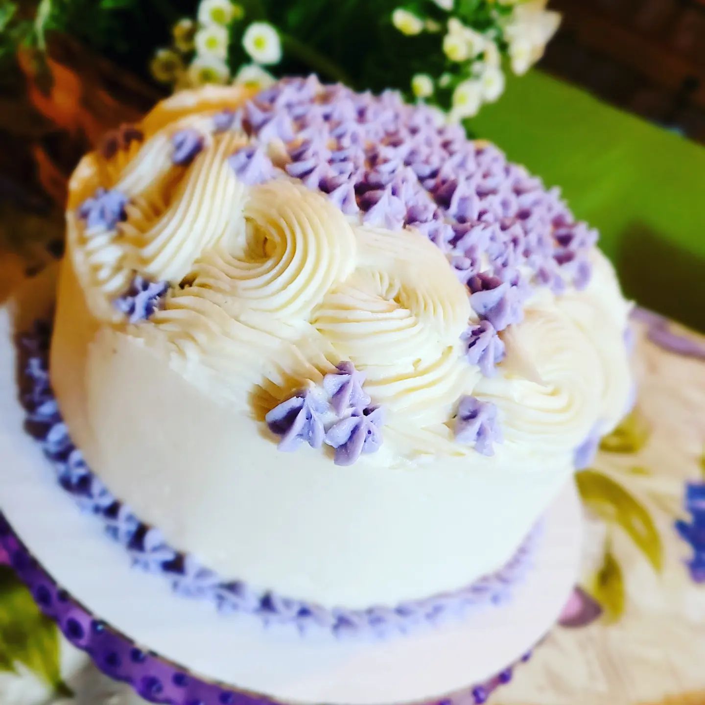 White cake with purple flower details made by Berries & Flour.