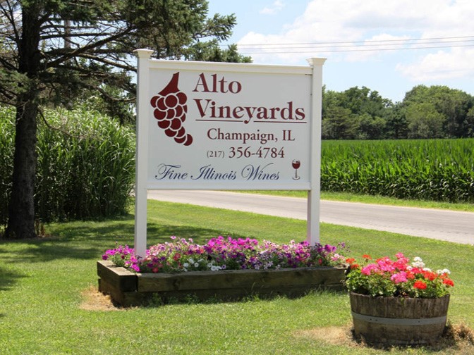 white Alto Vineyards sign with maroon text, surrounded by flowers