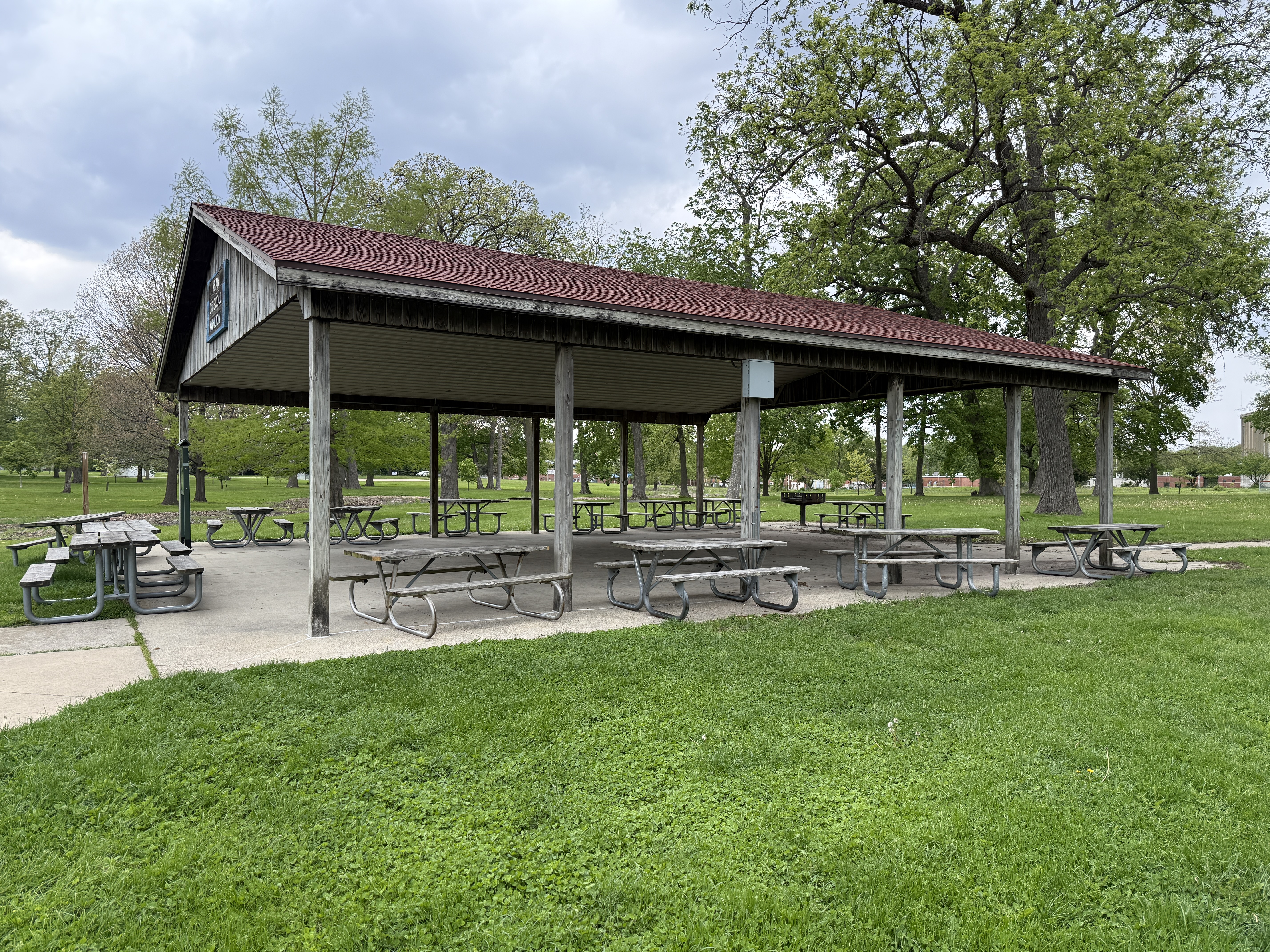 pavilion with a brown roof and wooden tables, surrounded by grass