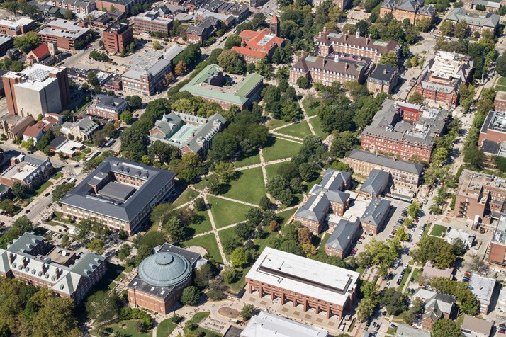 overhead view of a green space with X-shaped walkways, surrounded by college buildings