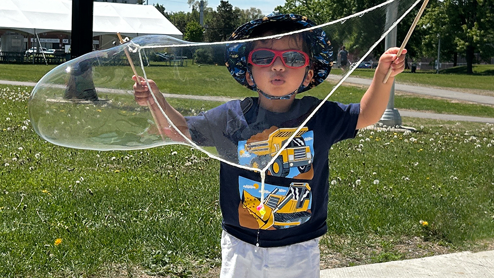 A young boy stands with a large bubble in his hands.
