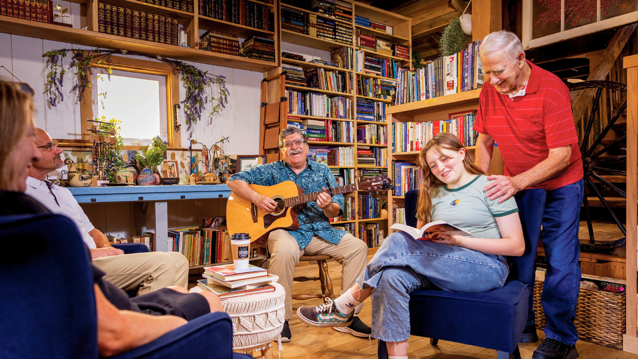 Papa’s Book Shoppe – Cortland Ohio Indie Bookstore Community scene inside Papa’s Book Shoppe in Cortland, Trumbull County, Ohio: customers relax among floor-to-ceiling shelves as a musician plays guitar in the cozy, wood-beam bookstore.
